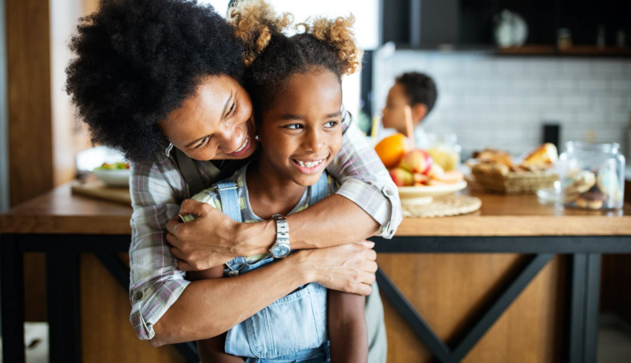 Shows mother embracing daughter inside a kitchen.